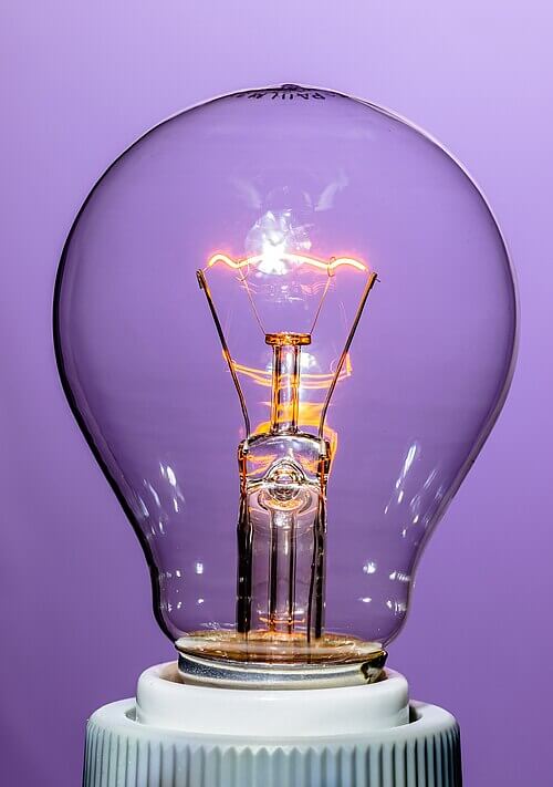 An incadenscent bulb with a glowing filament on a violet background.